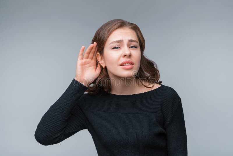 Young pretty brunette woman in casual black sweater holding hand near ear trying to listen something