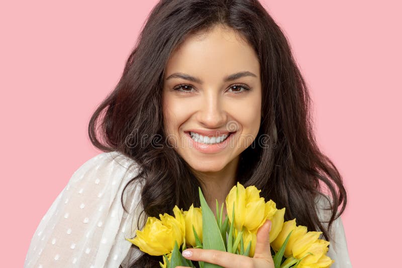 Young pretty dark-haired woman holding yellow flowers and smiling