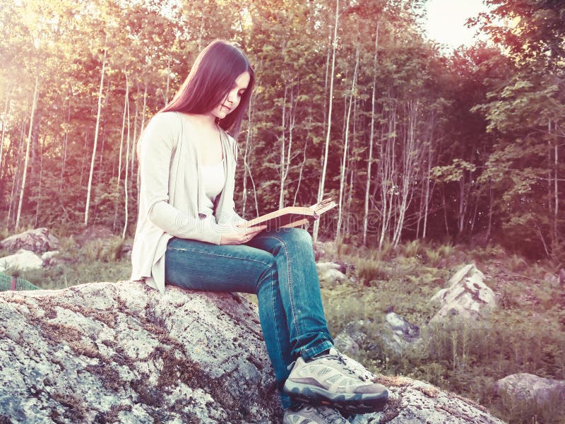 Young pretty girl reading a book sitting on a large rock in the forest royalty free stock photo Young pretty girl reading a book sitting on a large rock in the forest royalty free stock photo