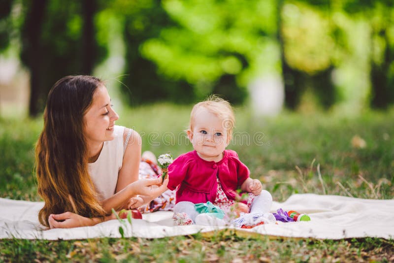 Young Pretty Mother With Daughter Lie On A Plaid In The Park. Family Outdoor Recreation. Family Summer Picnic In The Park. Mom And