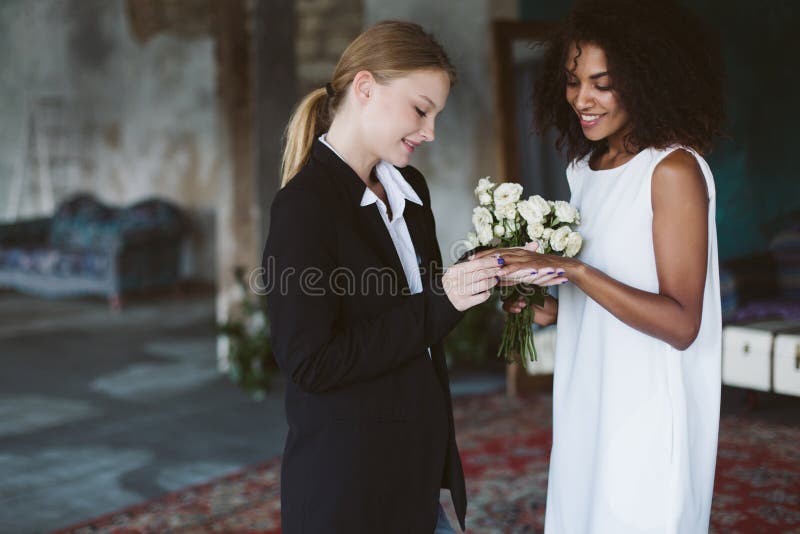 https://thumbs.dreamstime.com/b/young-pretty-woman-blond-hair-black-suit-putting-wedding-ring-beautiful-african-american-woman-dark-curly-hair-181873613.jpg