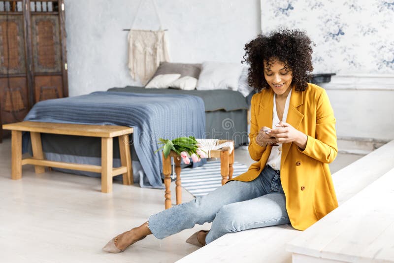 A young, pretty woman with curly hair, dressed in a jacket and jeans, sitting on the steps and looking at the phone stock photography A young, pretty woman with curly hair, dressed in a jacket and jeans, sitting on the steps and looking at the phone stock photography
