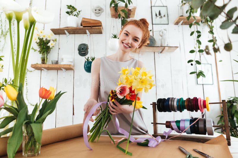 Young pretty woman looking camera while collecting bouquet in workshop