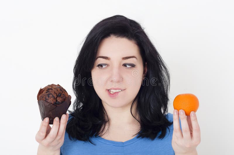 Young pretty woman making difficult choice between fruit and chocolate muffin. royalty free stock photography Young pretty woman making difficult choice between fruit and chocolate muffin. royalty free stock photography