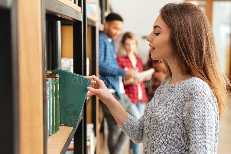 Young pretty woman student standing in library holding book. royalty free stock photos Young pretty woman student standing in library holding book. royalty free stock photos