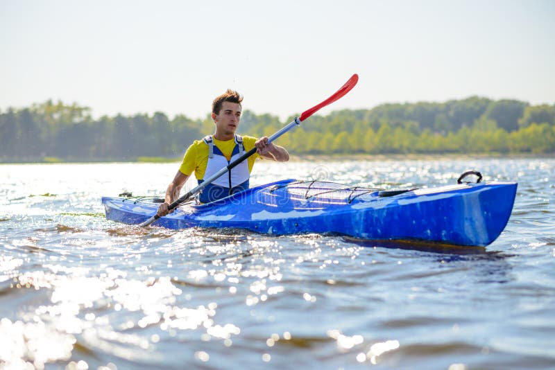 Young Professional Kayaker Paddling Kayak on River under Bright Morning Sun. Sport and Active Lifestyle Concept