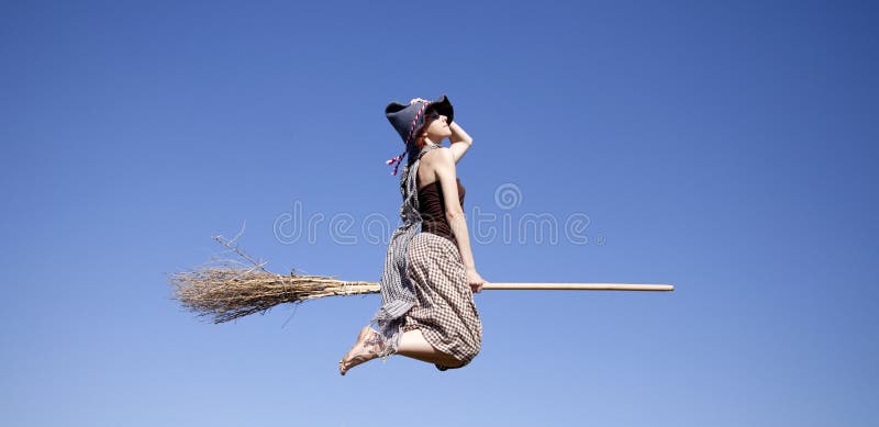 Young red-haired witch on broom flying in the sky