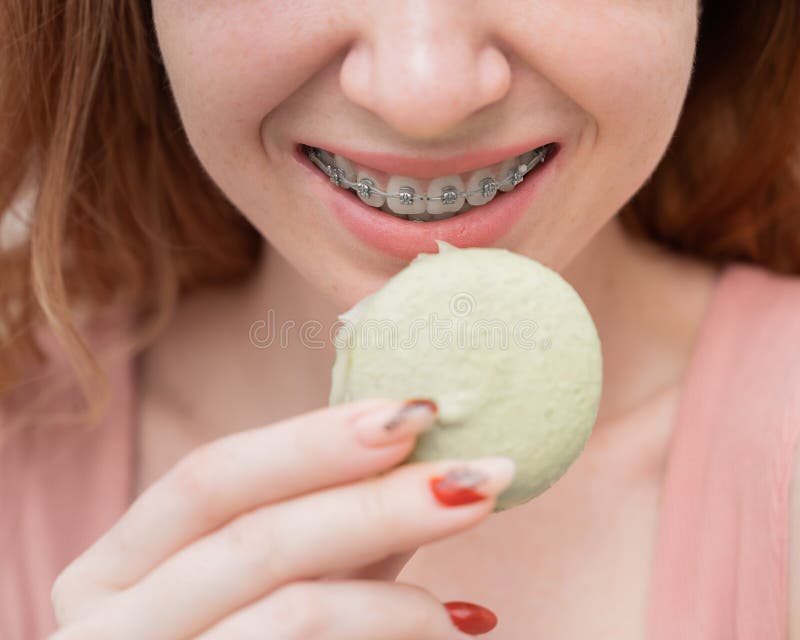 Young Redhaired Woman with Braces Eating Macaron Cake. Stock Image
