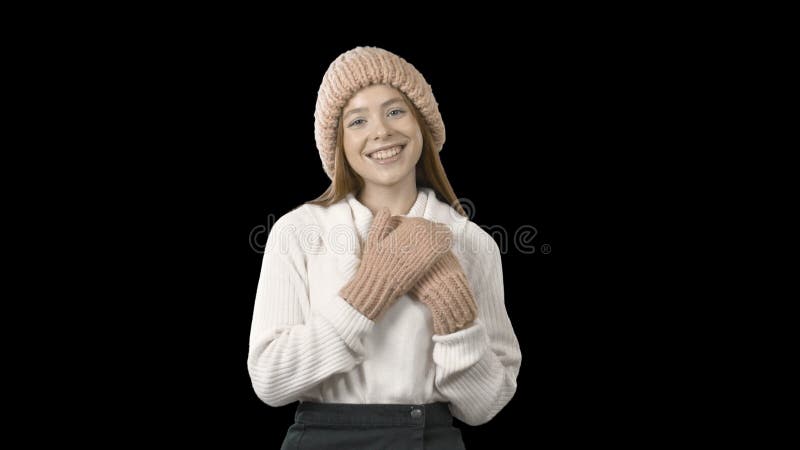 Young red-haired young lady in a knitted pink hat and mittens clasping her hands pleasantly surprised, fashion shooting