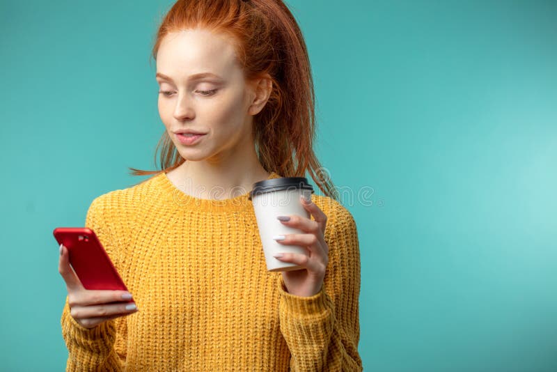 Young redhaired woman with coffee and smartphone isolated over blue background stock photos Young redhaired woman with coffee and smartphone isolated over blue background stock photos