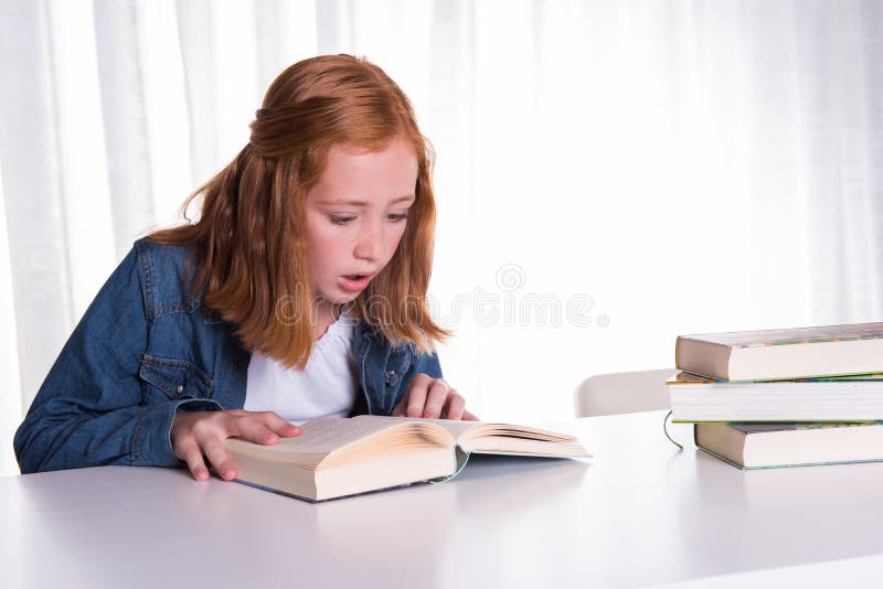 Young redhead girl reading in books - she is scared royalty free stock photography Young redhead girl reading in books - she is scared royalty free stock photography