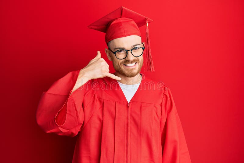 Young redhead man wearing red graduation cap and ceremony robe smiling doing phone gesture with hand and fingers like talking on