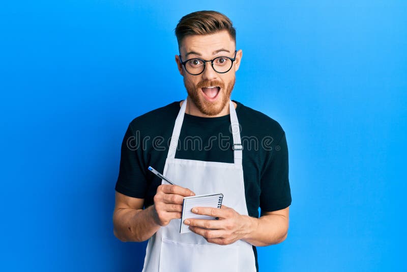 Young redhead man wearing waiter apron taking order celebrating crazy and amazed for success with open eyes screaming excited