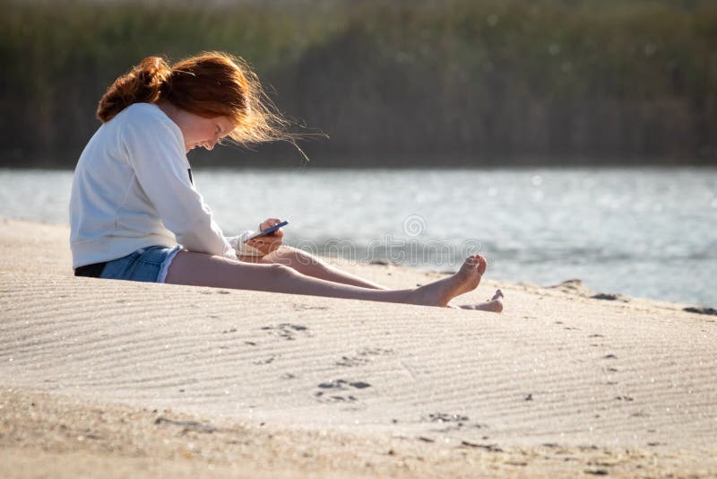 Young redheaded girl using a phone beside a river at the beach stock image Young redheaded girl using a phone beside a river at the beach stock image