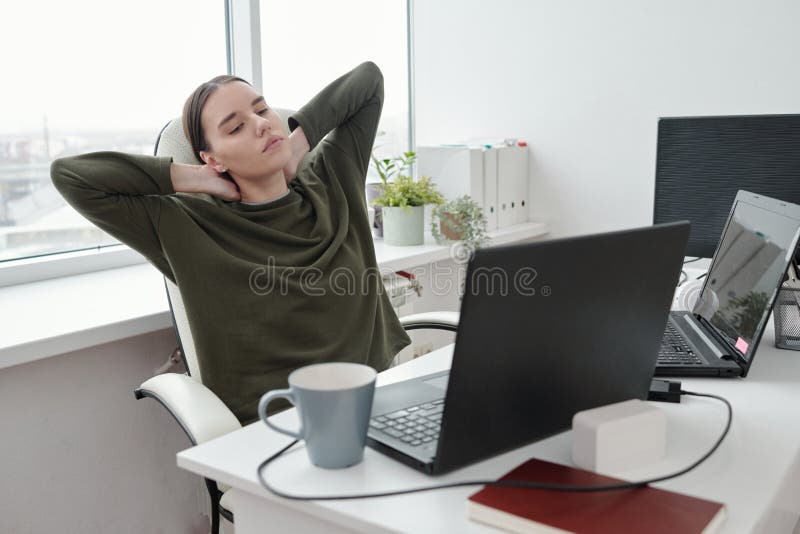 Young relaxed female programmer doing exercise for neck and arms by desk stock photo