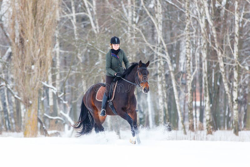Young woman galloping on bay horse on winter field