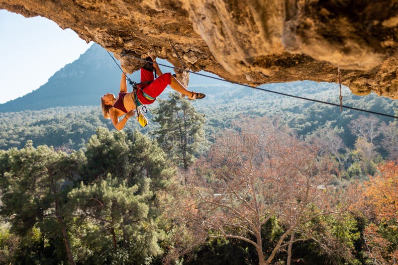 A young rock climber on an overhanging cliff. The climber climbs the rock. The girl is engaged in sports climbing