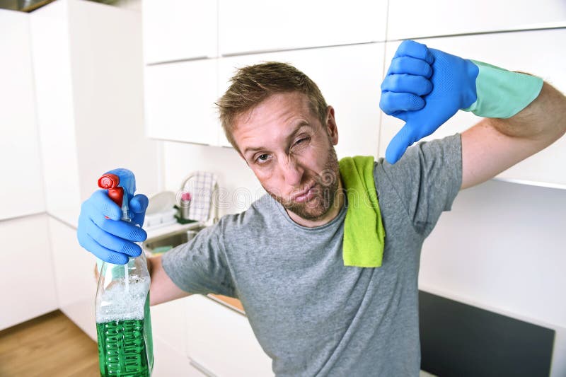 Young sad man in rubber gloves cleaning with detergent spray washing and ma...