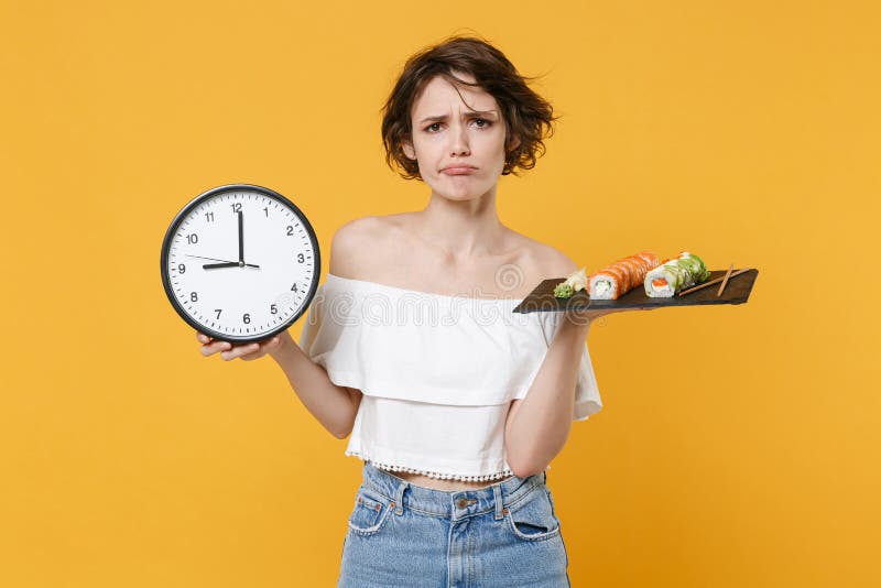 Young sad woman girl in casual clothes hold in hand clock makizushi sushi roll served on black plate traditional stock photos