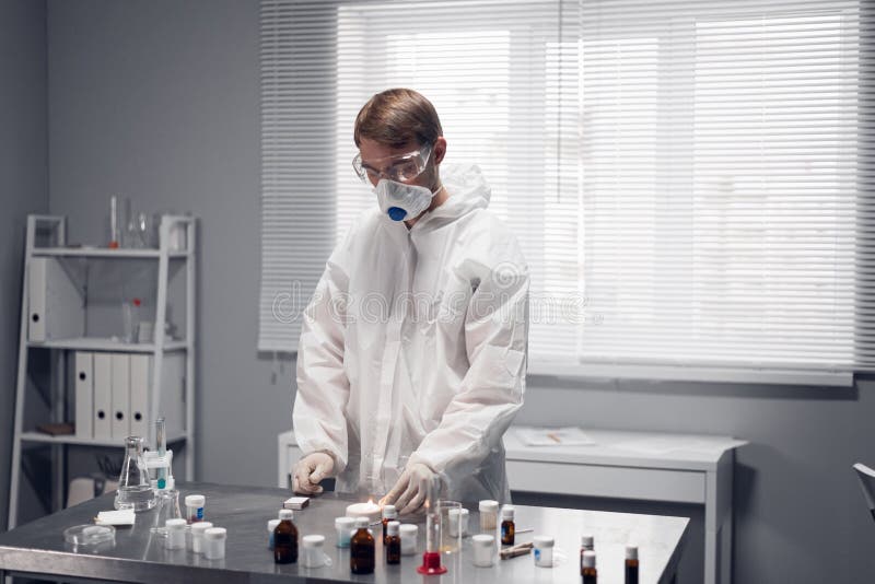 Young scientist in protective clothing and a respirator working in a chemistry laboratory, experimenting with heating royalty free stock photo