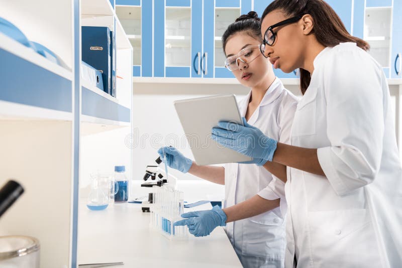 Young scientists using digital tablet while making experiment in chemical laboratory, scientists working together stock images