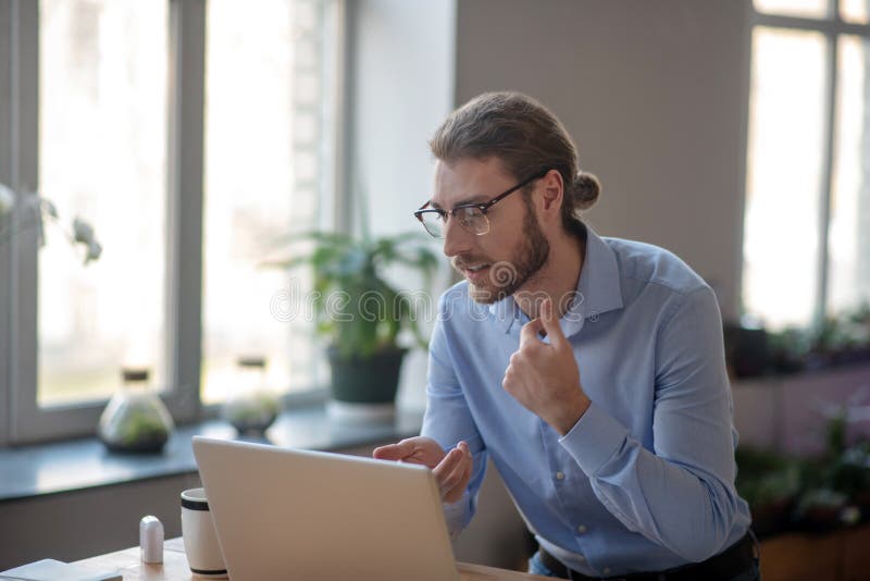 Young serious man talking online on laptop in office.