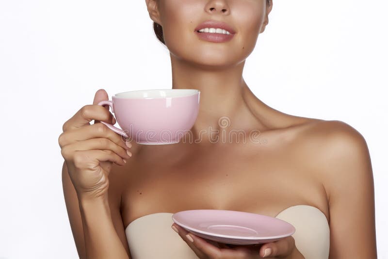 Young beautiful woman with dark hair picked up holding a ceramic cup and saucer pale pink drink tea or coffee on a white back