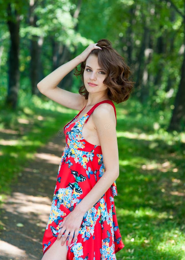 Young Brunette Girl in Red Dress Posing on Alley in Summer Park Against ...