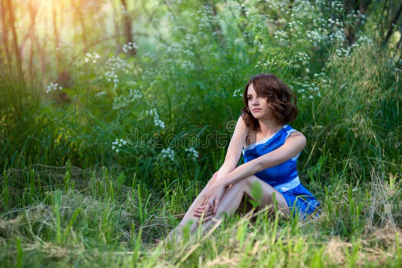 Young brunette girl in blue dress posing lying on grass in summer park stock images Young brunette girl in blue dress posing lying on grass in summer park stock images