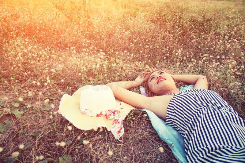 Young woman lying in grass nearing her hat look into the s