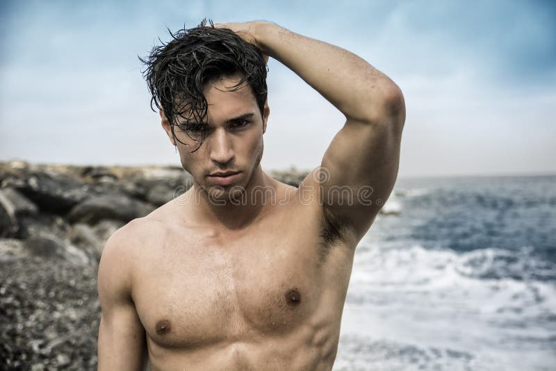 Young shirtless athletic man standing in water by ocean shore