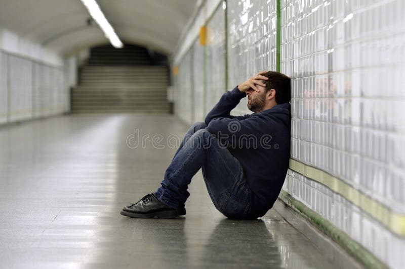 Young sick man lost suffering depression sitting on ground street subway tunnel