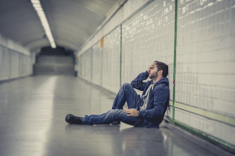 Young sick man lost suffering depression sitting on ground street subway tunnel