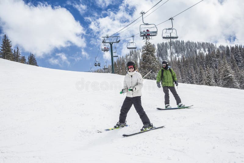 Young skier and a snowboarder skiing and boarding down a ski slope