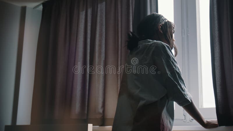 Young sleepy lonely woman looking through the window