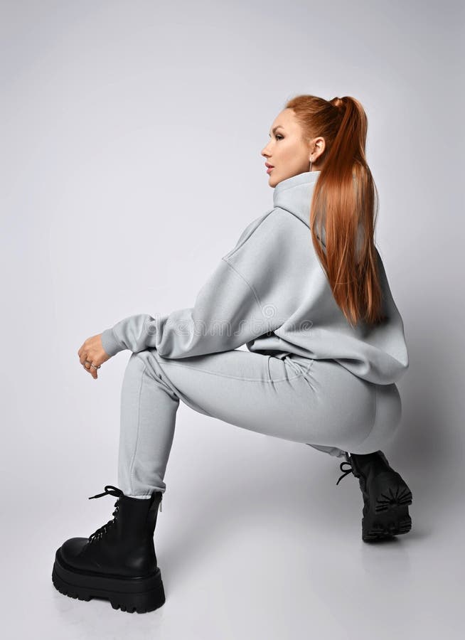 Young Slim Red-haired Woman in Sportswear Hoodie, Pants and Black Massive  Shoes Sits Squatted Back To Camera Stock Image - Image of earring, pants:  232281375