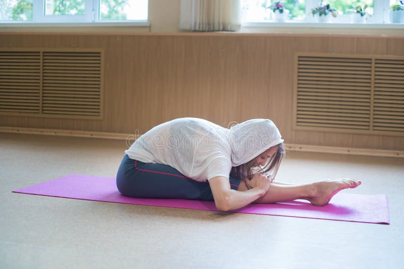 Young slim woman in the white hood sitting on the yoga mat with