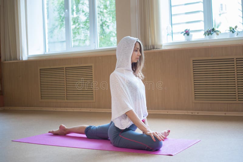 Young slim woman in the white hood sitting on the yoga mat with