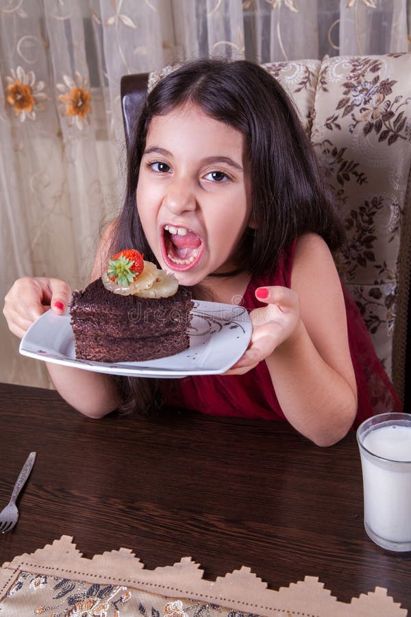 Young small beautiful middle eastern child girl with chocolate cake with pineapple, strawberry, and milk with red dress and dark