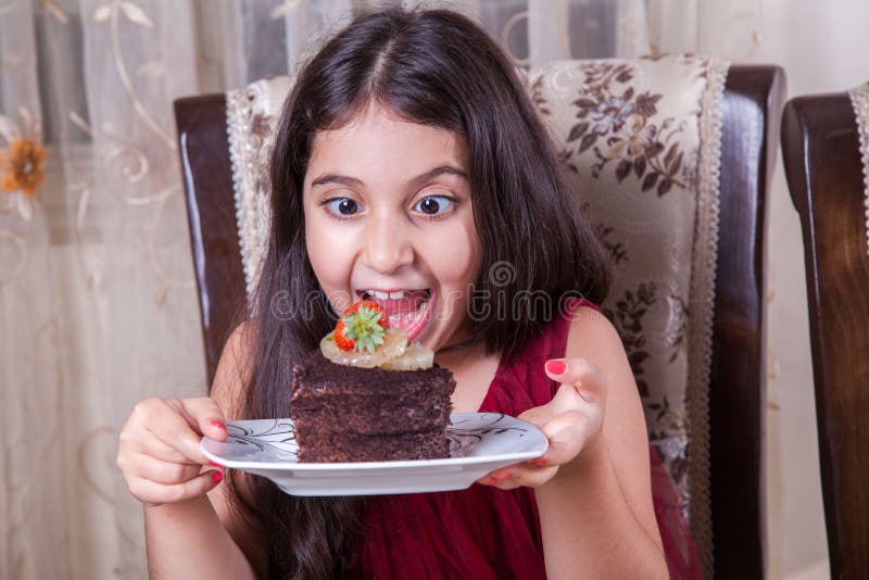 Young small beautiful middle eastern child girl with chocolate cake with pineapple, strawberry, and milk with red dress and dark