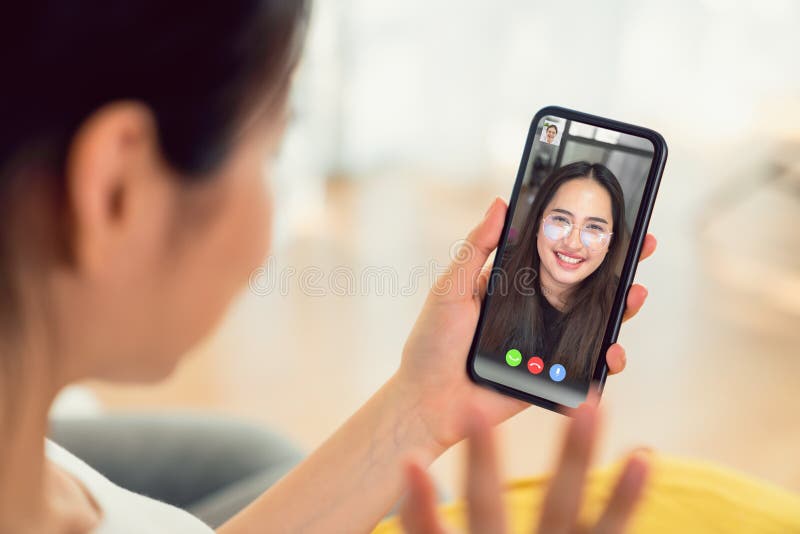 Young smiling Asian woman making video call online talking with friends to smartphone from home.