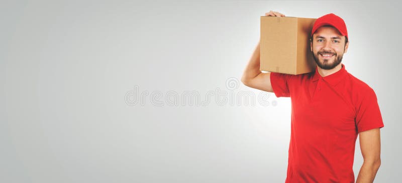 Young smiling delivery man in red uniform and with shipment box on shoulder royalty free stock images