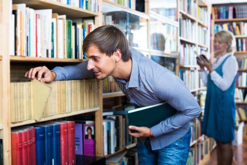 Young Smiling Man Looking for New Book on Shelves Stock Photo Image of picking, bookshelf
