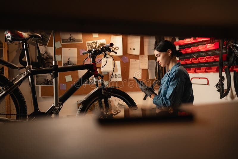 Young smiling mechanic girl using mobile phone in bike repair workshop. Concept of taking break time and reading stock images