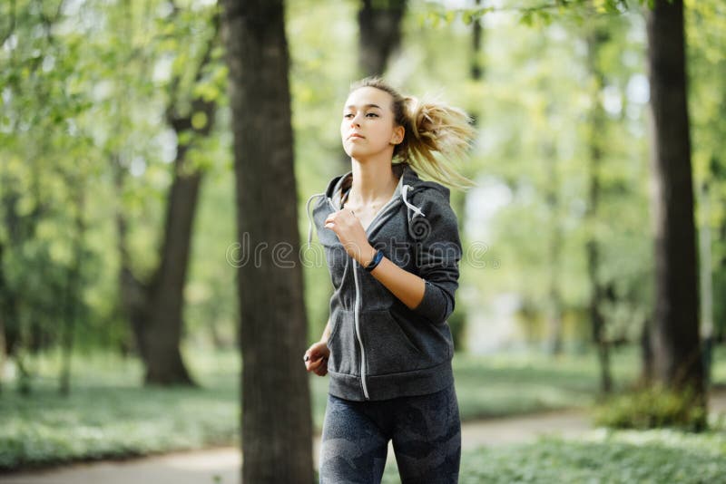 Young smiling sporty woman running in park in the morning. Fitness girl jogging in park