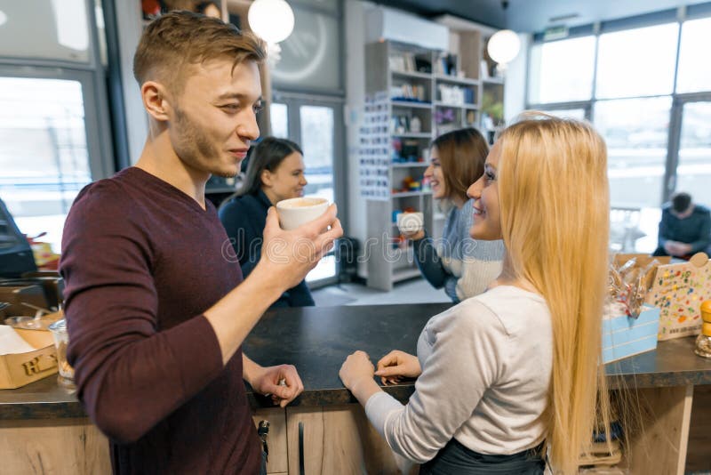 Young smiling and talking barista working at coffee shop behind the bar counter with cup of fresh coffee. Teamwork, staff, people royalty free stock photography Young smiling and talking barista working at coffee shop behind the bar counter with cup of fresh coffee. Teamwork, staff, people royalty free stock photography