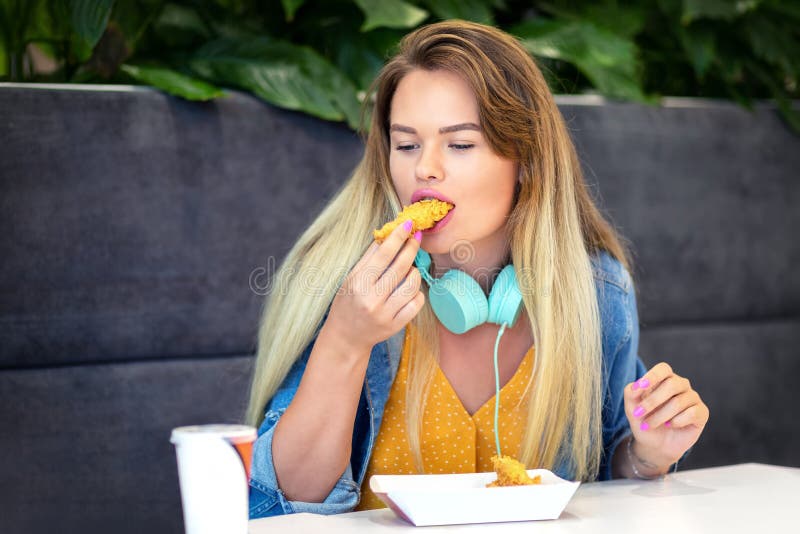 Young smiling trendy woman eating crispy strips or fried chicken at fast food stock photos Young smiling trendy woman eating crispy strips or fried chicken at fast food stock photos