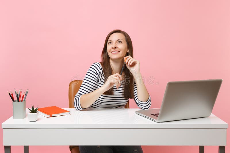 Young smiling woman holding pencil looking up thinking dreaming sit work at white desk with contemporary pc laptop stock photo Young smiling woman holding pencil looking up thinking dreaming sit work at white desk with contemporary pc laptop stock photo