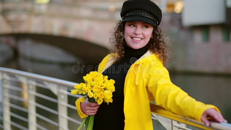 Young smiling woman in a yellow raincoat with daffodils outdoors