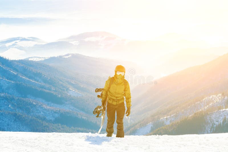 Young snowboarder climbing up the mountain with his board in hand at golden hour